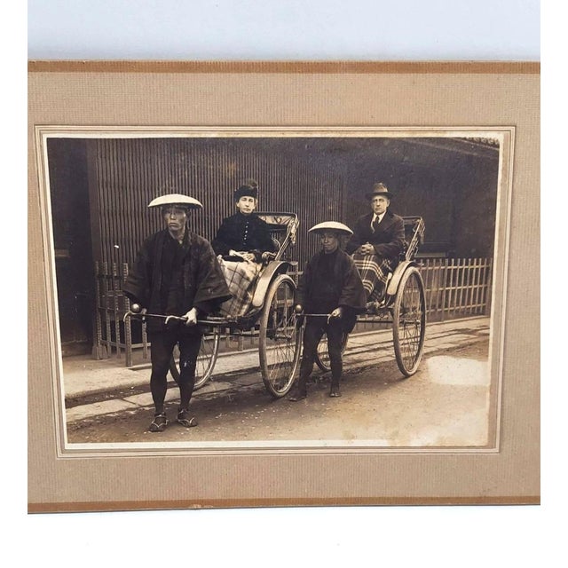 An American or European couple rides side by side in rickshaws. Both tucked in under wool blankets. Japanese men in...