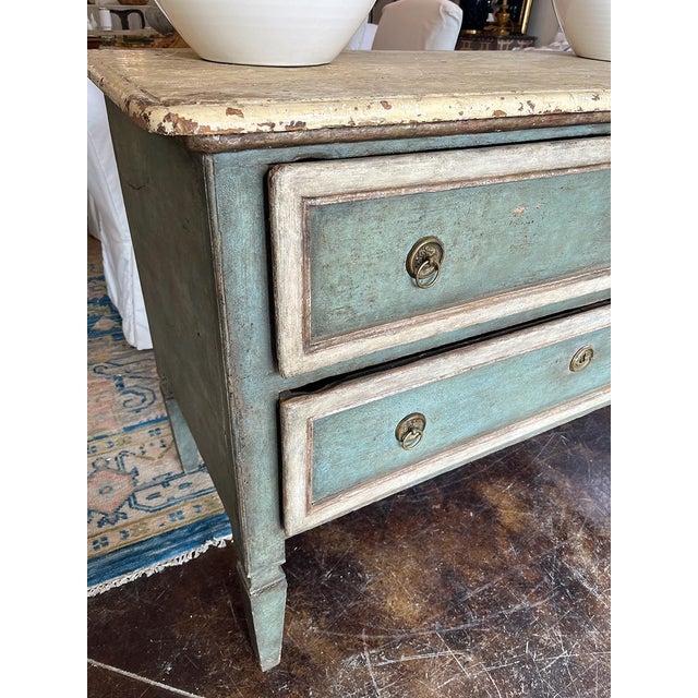 This 18th-century chest is painted in a blue-green shade and white. It has two drawers, each with a lock and two pulls....