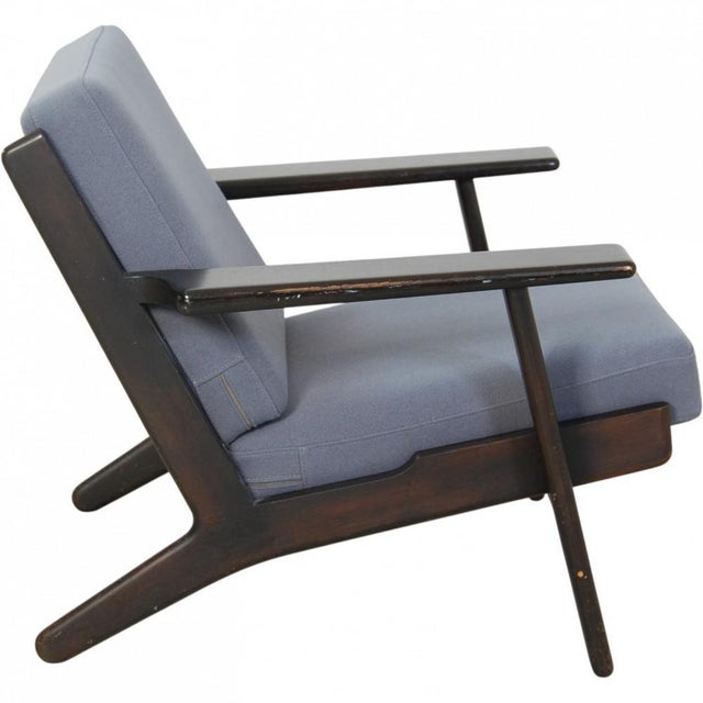 Hans Wegner GE290 lounge chair with a frame of black painted oak and cushions upholstered in blue fabric. The chair is...