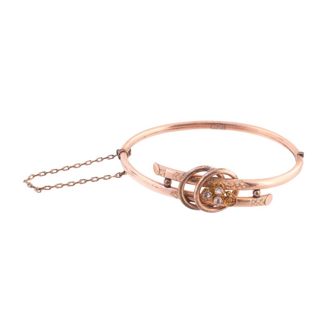 The bangle bracelet features a gold-filled design with intricate detailing. The centerpiece showcases rhinestones arranged...
