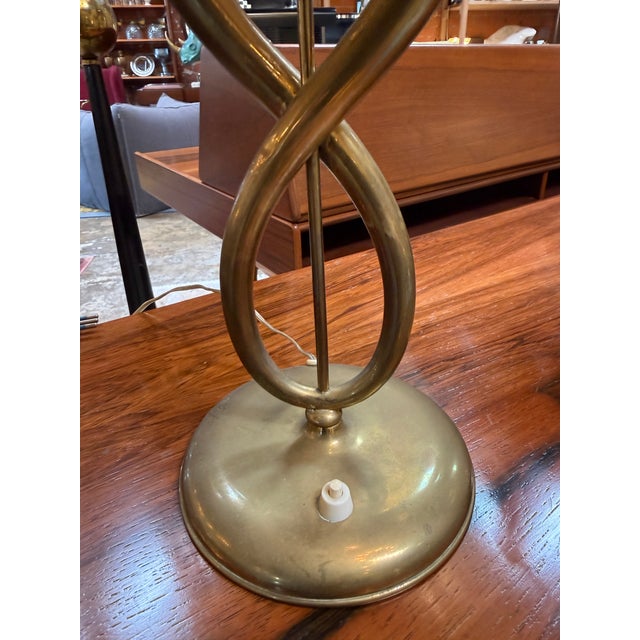 Elegant Italian table lamp from the 1950s, defined by its sculptural brass base composed of two curved arms that...
