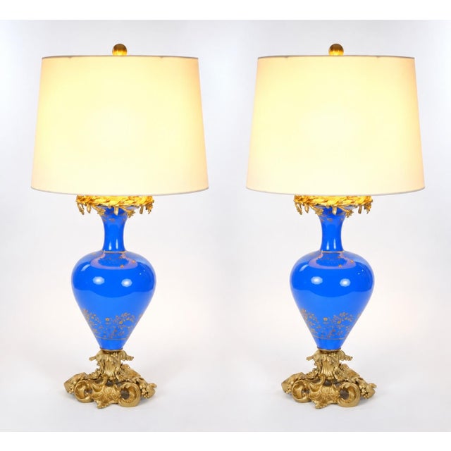 This elegant pair of antique table lamps features richly colored blue glass bodies, complemented by finely cast gilt...