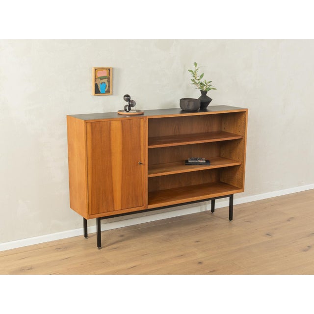 Classic sideboard from the 1950s. Walnut veneer body with one cabinet door, four shelves, and new square steel feet in...