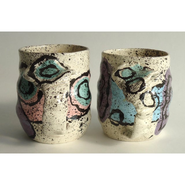 A pair of vintage hand formed pottery mugs with 80s modern decorations in mint, pink, purple, blue and black.