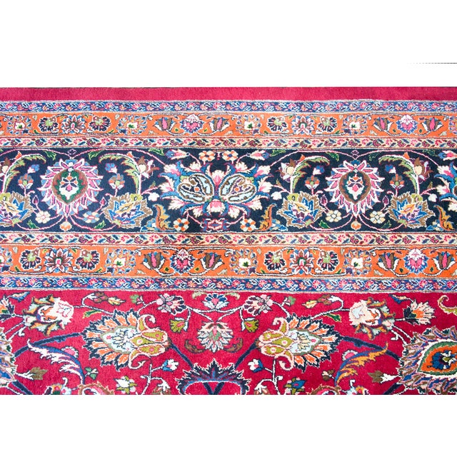 This mid-20th-century Persian Meshed rug features a vibrant red field adorned with an intricate all-over floral pattern...