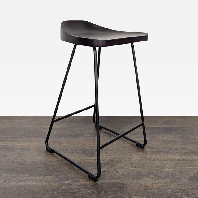 This Pottery Barn counter stool features a sleek, curved wood seat and sturdy black metal legs. The modern, minimalist...