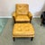 A wonderful 1970's yellowish tan colored vinyl and walnut chair and matching ottoman with padded buckle armrests. This is...