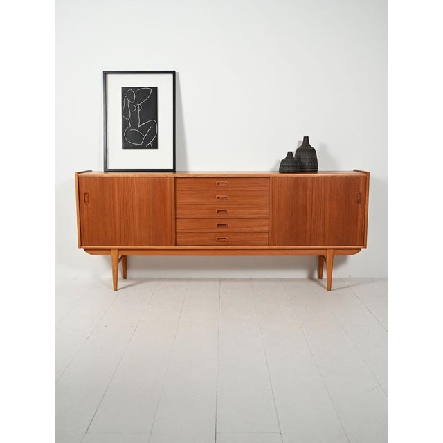 Two-tone teak sideboard with sliding doors and a row of central drawers, carved handles, and a slender profile on slender...