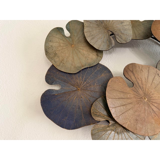 Sculptural metal wall art featuring an overlapping arrangement of lotus or lily pad leaves in beautifully muted shades of...