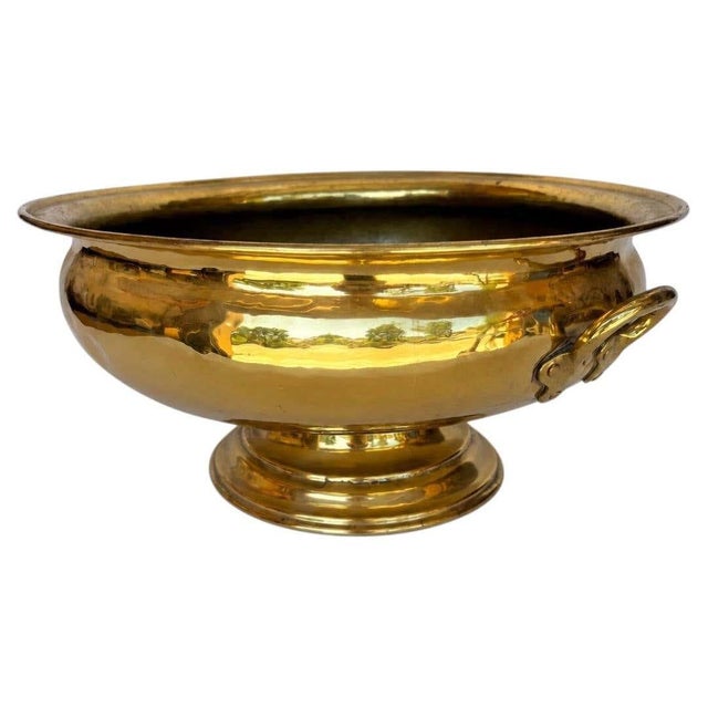 Substantial early 20th-century footed brass bowl with decorative ring handles, distinguished by its broad rounded body,...