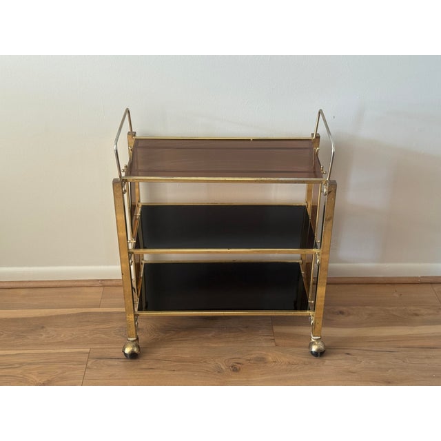 Vintage three-tier bar cart featuring a gold-tone metal frame, smoked plastic shelves.