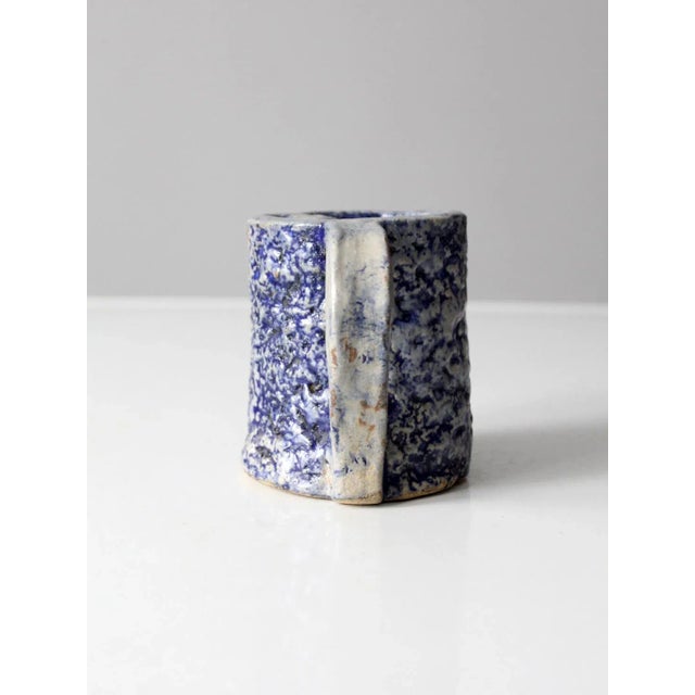 This is a vintage studio pottery mug. Signed by the artist, the rustic handmade mug has a textured blue and white glaze....
