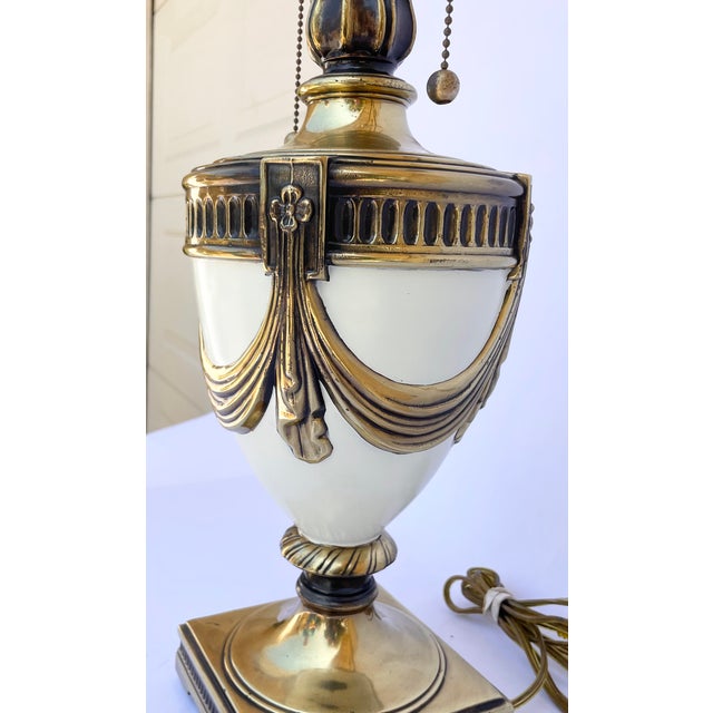 A striking vintage table lamp featuring a substantial cream enamel urn raised on a square pedestal base and adorned with...