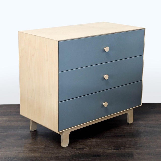 This Ouef dresser features a clean, modern design with a blue front and natural wood sides and top. It has three spacious...