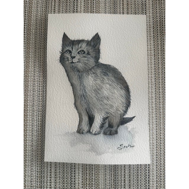 An original hand-painted watercolor featuring a softly rendered gray kitten with expressive eyes and delicate fur...