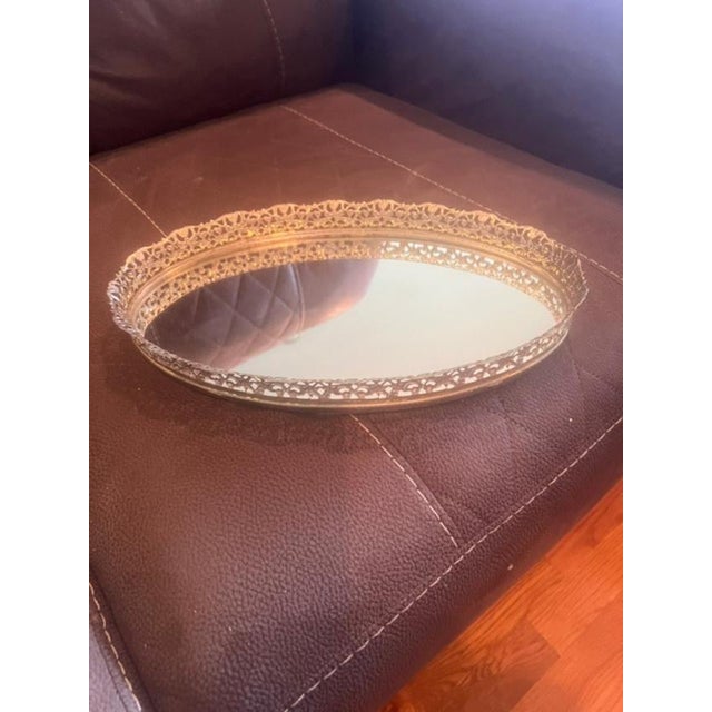 This elegant vintage vanity tray features an oval mirrored base surrounded by an intricate gold-tone metal filigree...