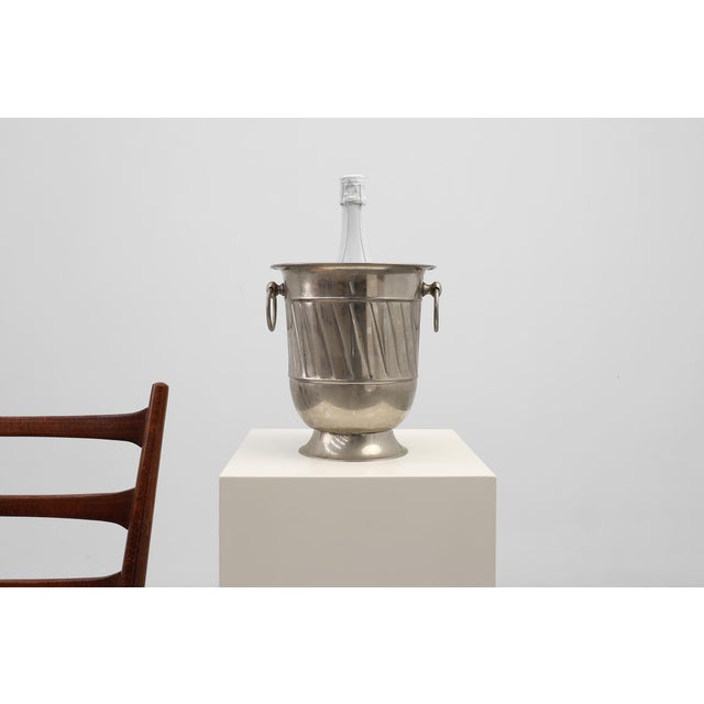 A refined Art Deco metal ice bucket distinguished by its clean geometry, polished surface, and sculptural ring handles...