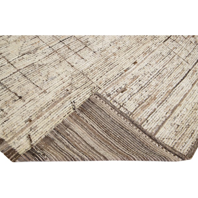 Beautiful Moroccan-style handmade wool rug with a beige color field. This Modern rug has brown accents featuring a...