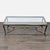 This designer glass top table with patinaed cabriole iron legs, stretcher, and gilded top edging is in the Hollywood...