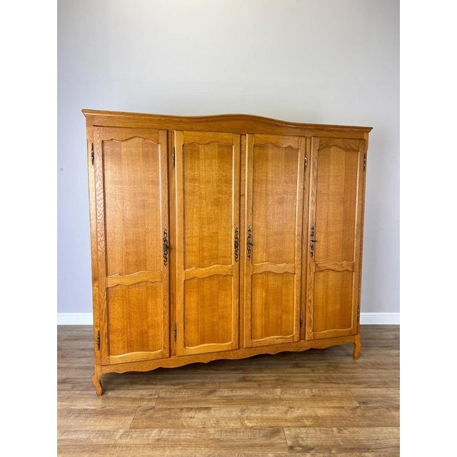 An elegant Vintage French Louis wardrobe in oak, featuring four panelled doors, a gently shaped upper profile, decorative...