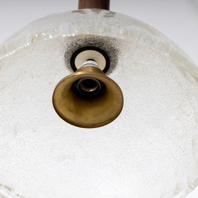 Ceiling lamp with glass shade and wooden shaft. The upper end is surrounded by an irregular bronze relief, signed...