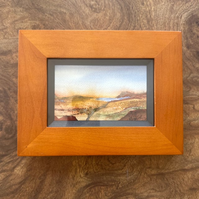 This framed watercolor landscape evokes the quiet majesty of a desert horizon. Warm earthy tones blend with distant blues...