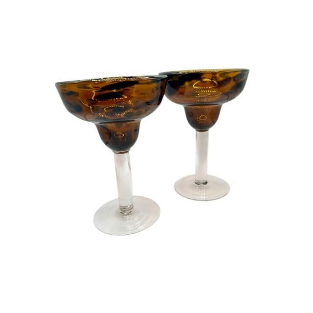Add flair to your home bar with this striking pair of hand-blown tortoise shell margarita glasses. Crafted with an eye-...