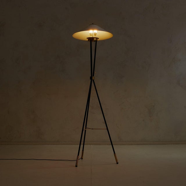 A 1950s Italian floor lamp with a sculptural tripod silhouette. The white-lacquered aluminum shade flares outward in a...