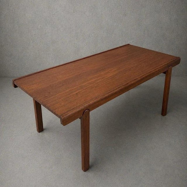 A clean-lined Danish mid-century teak coffee table with a rectangular top, softly rounded edges and elegant cylindrical...