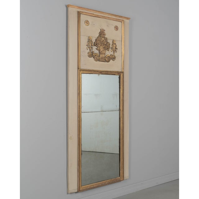 An early 20th century French Louis XVI style trumeau mirror with painted pine frame and gilded trim. Carved giltwood...