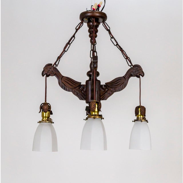A dark walnut-stained wood chandelier in a 4-arm structure of basic, stylized, hand-carved birds that come together at the...