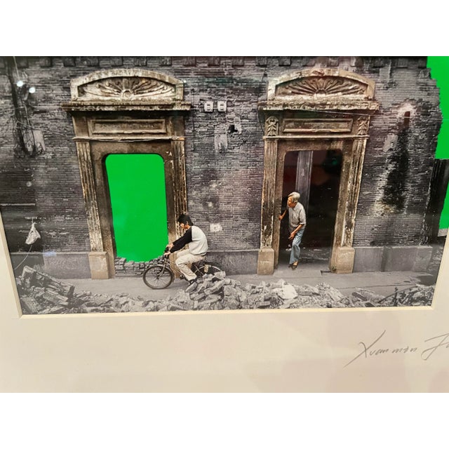 This is a striking photograph of a young man on a bicycle set before a dilapidated building in Southeast Asia. The emerald...