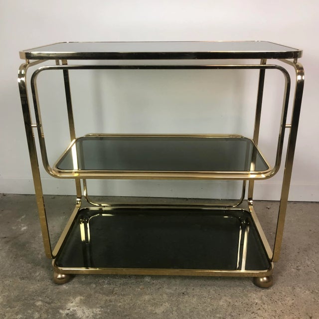 Large trolley / rolling table in gold metal with three shelves of smoked glass platforms. 4 casters. Vintage Italian...