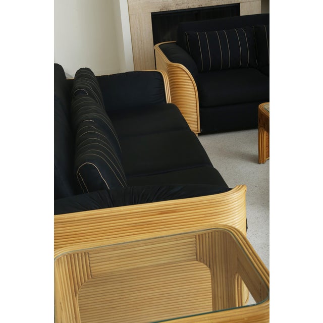 A sculptural side table crafted from reeded rattan with softly rounded corners and an inset glass top. Arched legs and a...