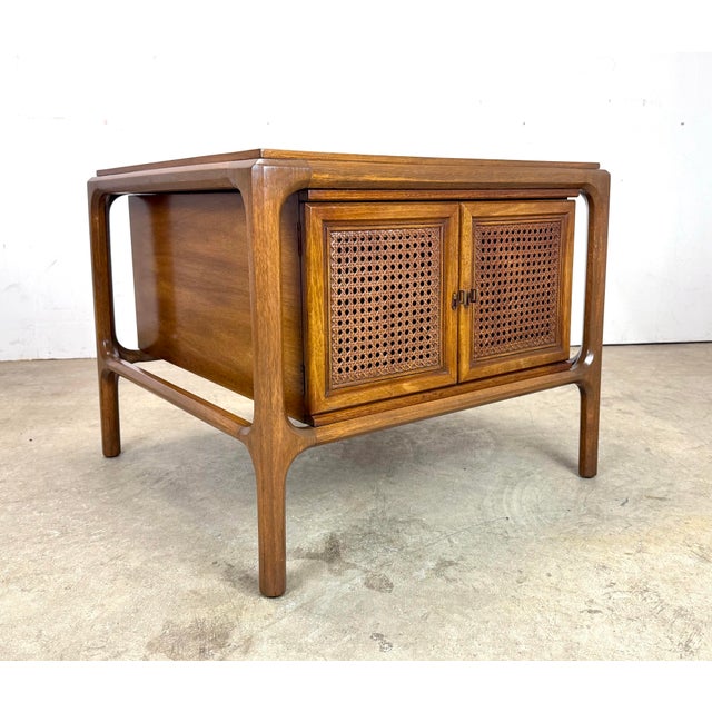 A sculptural mid century modern side table in walnut by McGuire (unsigned) circa 1960’s. Features two caned cabinet doors...