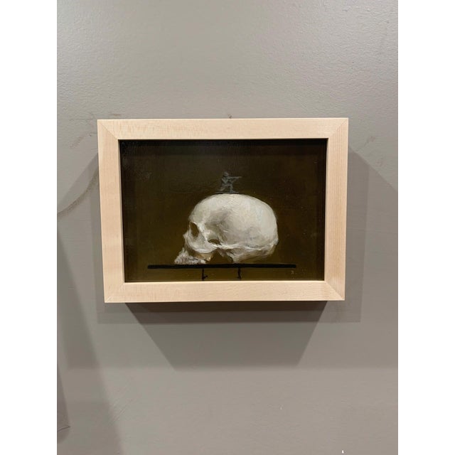 This artwork presents a striking juxtaposition of a skull and a small soldier figurine perched atop it, creating a...
