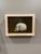 This artwork presents a striking juxtaposition of a skull and a small soldier figurine perched atop it, creating a...