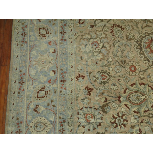 An oversize Persian Meshed rug with an all-over formal design on a tan field, an icy blue border, accent colors in red...