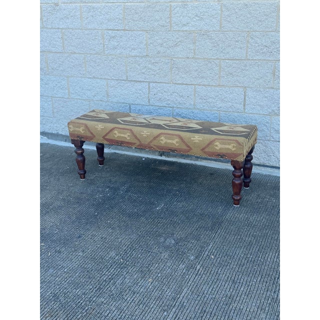 Rectangular upholstered bench with a padded seat covered in a kilim-style woven fabric. Textile features geometric motifs...