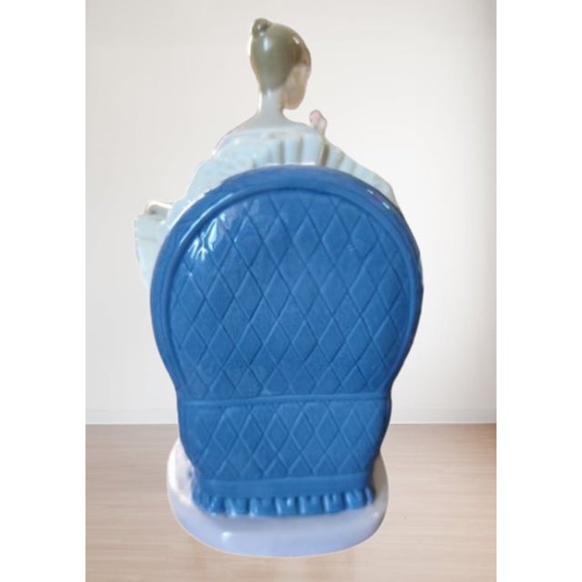 This is a porcelain piece by nao, a company belonging to the lladró group. It depicts a ballerina seated in a blue chair,...