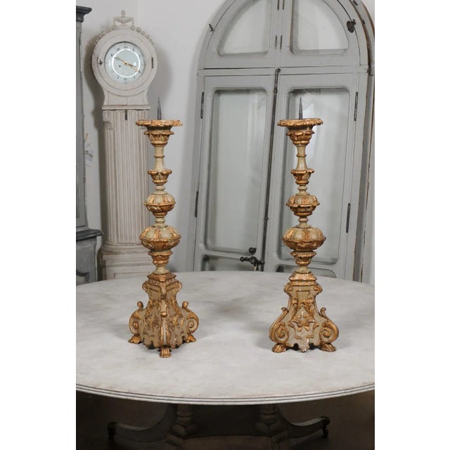 A pair of French Rococo style painted and carved wooden candlesticks from the 19th century, with gilt accents. Created in...