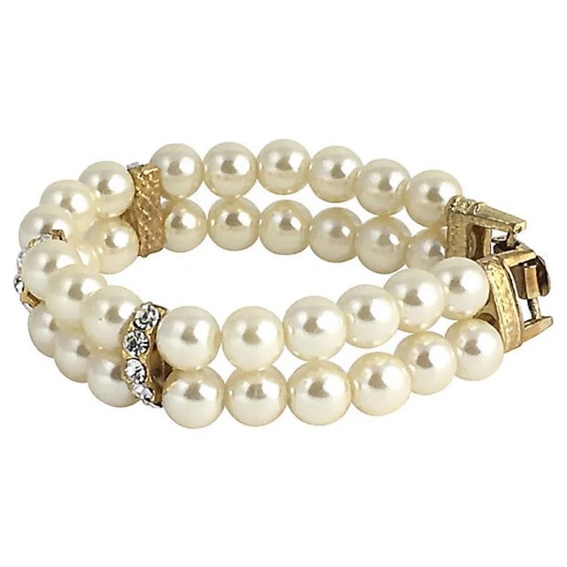 Double-strand faux-pearl bracelet interspersed with three spacer bars set with five rhinestones each. The goldtone metal...