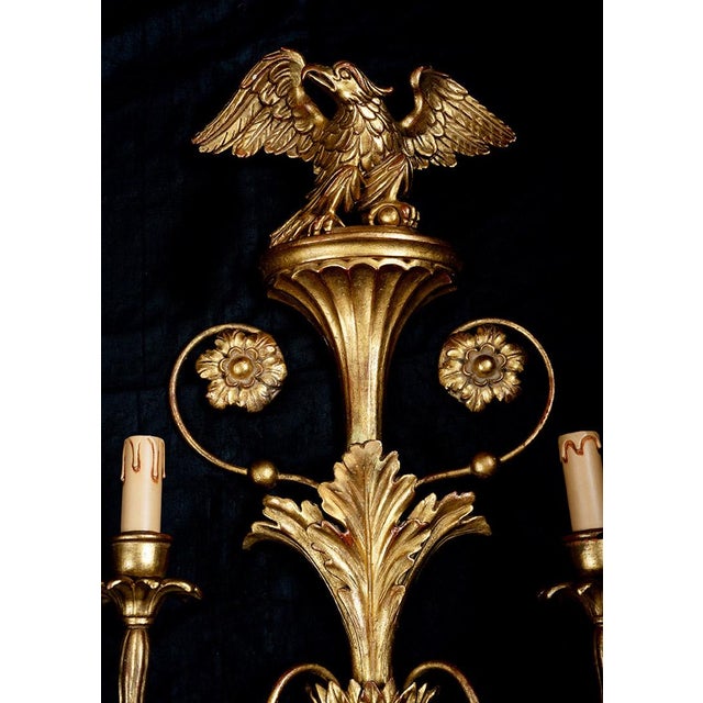 A pair of French wall sconces made of gilded, carved wood dating from the early 20th century. The central element is...