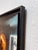 This oil on canvas piece captures a moment of transition as a figure steps out from a dimly lit interior into a softly...