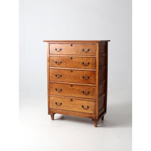 An early 20th-century American highboy dresser by the Spiegel Furniture Company, crafted in warm oak with natural tonal...