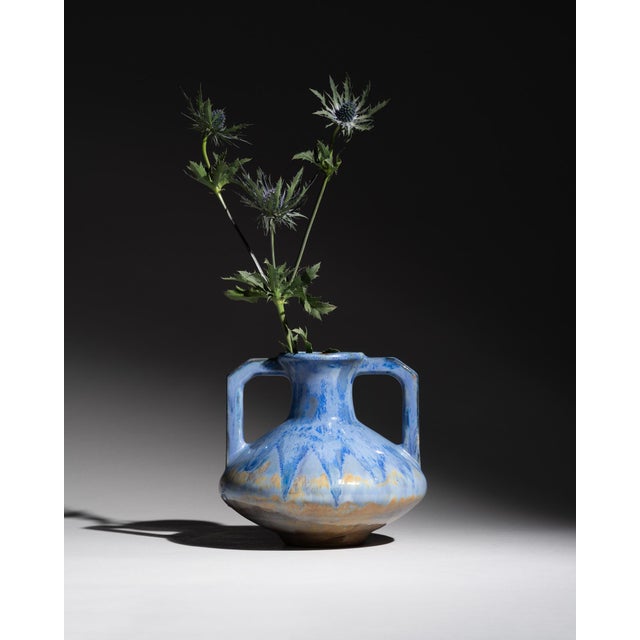 A French art pottery vase with angular twin handles and a flowing blue-grey crystalline glaze. The elongated amphora form...