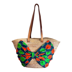 A Giselle Handwoven Straw Basket / Tote Featuring a Large Bow Made From Colorful Print and Brown Leather Shoulder Straps.