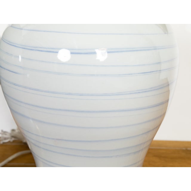 A pair of Asian white porcelain table lamps with hand-applied blue striated lines, each featuring a softly curving...