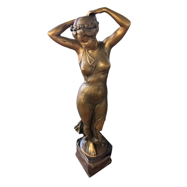 Elegant vintage figural sculpture depicting a graceful young woman standing in a flowing gown, her arms raised as she...