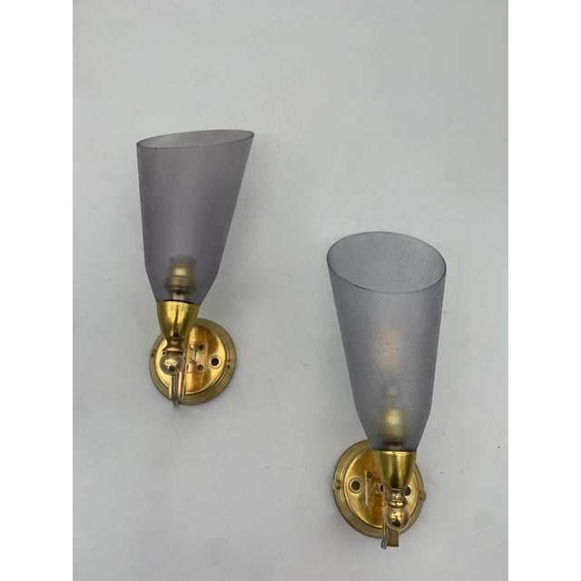 A pair of wall lamps with a brass base and arm, featuring a curved structure with a spherical element near the lamp...